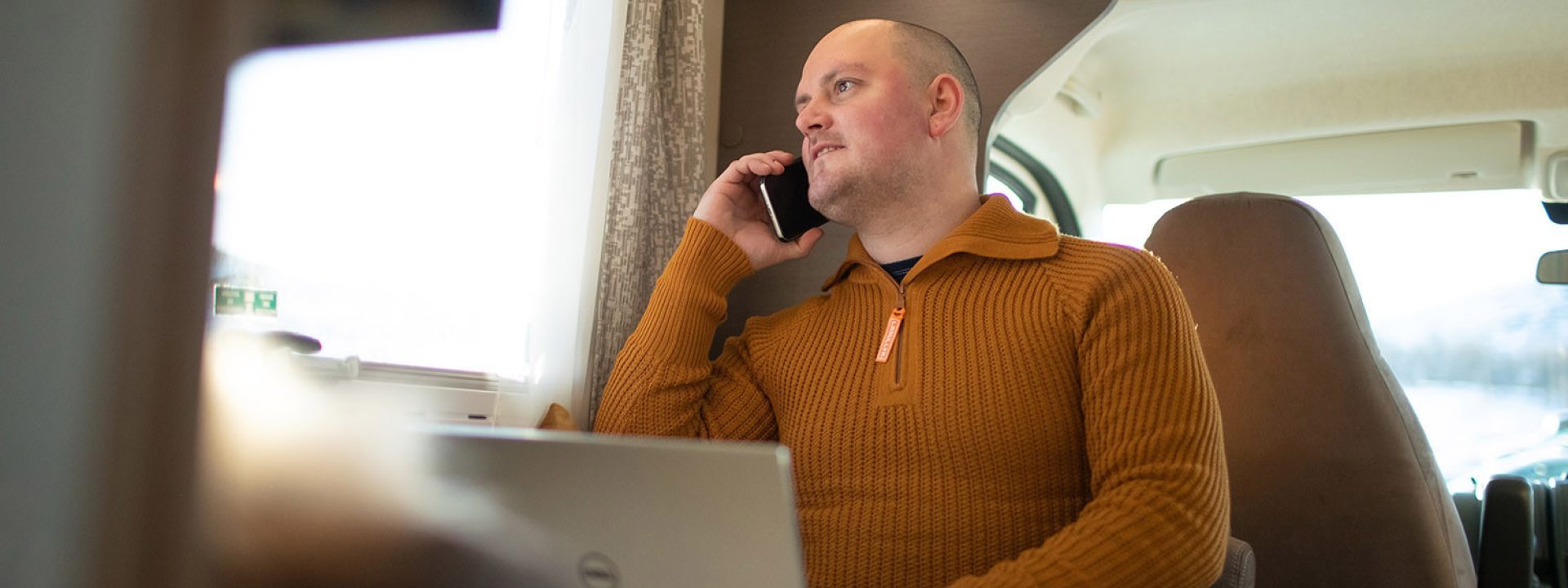 Mann som sitter med PC og telefon i bobil