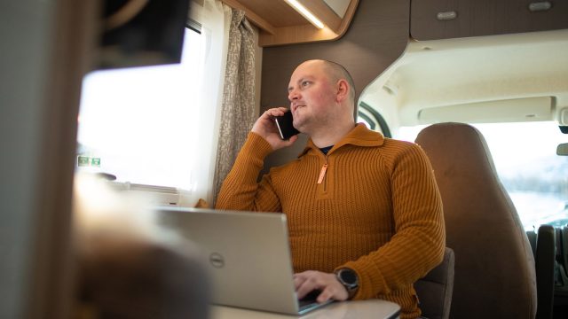Mann som sitter med PC og telefon i bobil