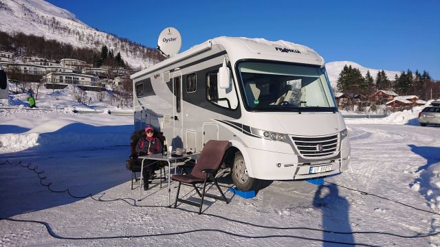 Kvinne sittende i foran bobil i snølandskap